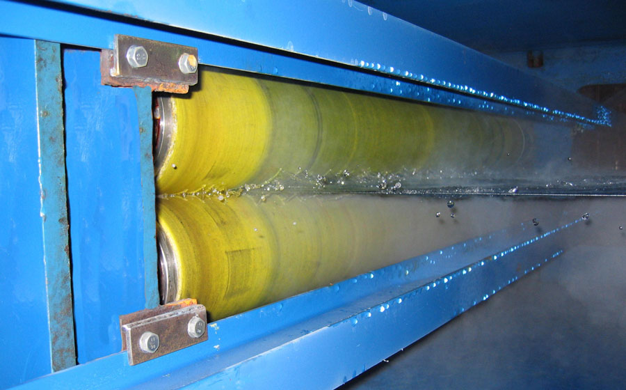 Two NCCM<sup>®</sup> Premier Yellow rolls wringing steaming hot liquid off of a piece of sheet metal running through a blue machine